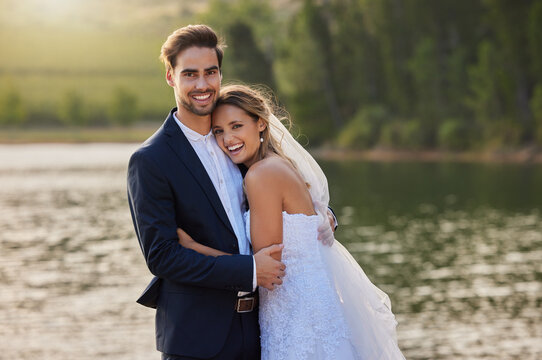 Happy wedding couple, portrait and hug by lake for romantic honeymoon getaway in nature. Man and woman hugging in happiness for marriage relationship or loving embrace in commitment in the outdoors