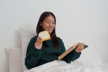 Pretty smiling young asian woman relaxing at home on bed and reading book. Lifestyle concept