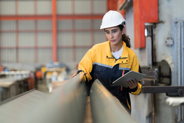 Metalwork manufacturing, warehouse of raw materials. Female factory worker inspecting quality rolls of metal sheet in factory during manufacturing process, wearing safety uniform, use digital tablet