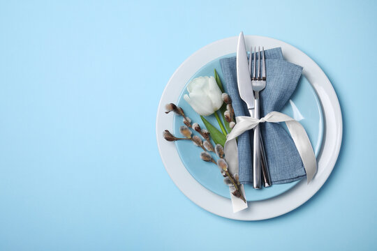 Wall Mural - Festive table setting with willow twigs and tulip on light blue background, top view with space for text. Easter celebration