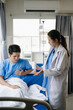 © Nuttapong punna - Doctor and young male patient who lie on the bed while checking pulse, consult and explain with nurse taking note in hospital