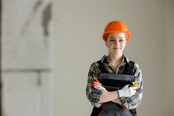 Portrait of a young professional woman electrician in a hard hat and overalls holding pliers for work, on a gray background