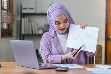 Wall Mural - Portrait of a beautiful Muslim millennial Asian businesswoman wearing a purple hijab working remotely from her home office.