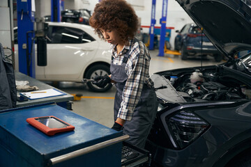 Canvas Print - Young auto repair worker in plaid shirt stands near car