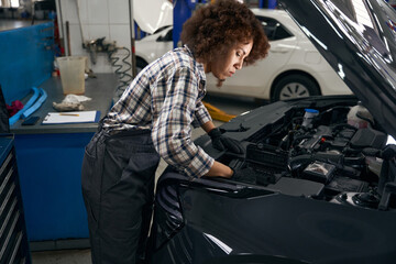 Canvas Print - Young woman checks the engine under hood of a car