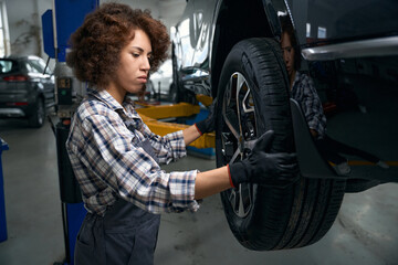 Canvas Print - Woman auto mechanic carefully examines a car wheel