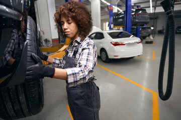 Canvas Print - Young curly woman repairman inspects a car wheel