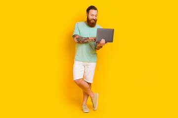 Wall Mural - Full body photo of cheerful young man use wireless netbook write email isolated on yellow color background