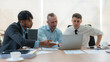 © amnaj - Group of diverse businessman going over paperwork together and working on laptop at meeting.
