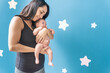 Young woman lovingly holding her baby who has an umbilical hernia on a blue background with stars