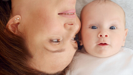 Wall Mural - Happy newborn baby with his mother. Healthy newborn baby in a white t-shirt with mom. Closeup Faces of the mother and infant baby. Cute Infant boy and parent, top view. Happy family portrait