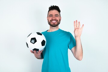 Sticker - Young man holding a ball over white background showing and pointing up with fingers number four while smiling confident and happy.