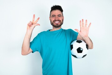 Sticker - Young man holding a ball over white background showing and pointing up with fingers number eight while smiling confident and happy.