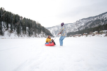 Couple having fun on winter vacation, tube in snow, while spending time outdoors on snowy winter day in mountains