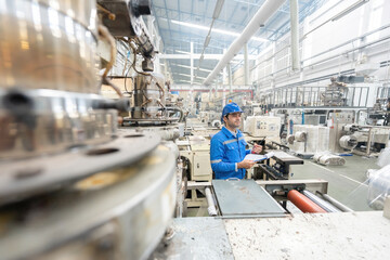 Wall Mural - European white male engineer standing working in the factory Holding a walkie-talkie and a listnote. Around there are machines working. Wear uniforms and wear helmets.