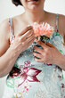 Mature woman wearing floral print dress holding beautiful peony flower. No face visible. Female power and sensitivity. Thyroid and health problems