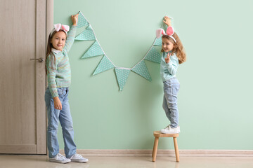 Wall Mural - Little girls in bunny ears hanging Easter flags on green wall