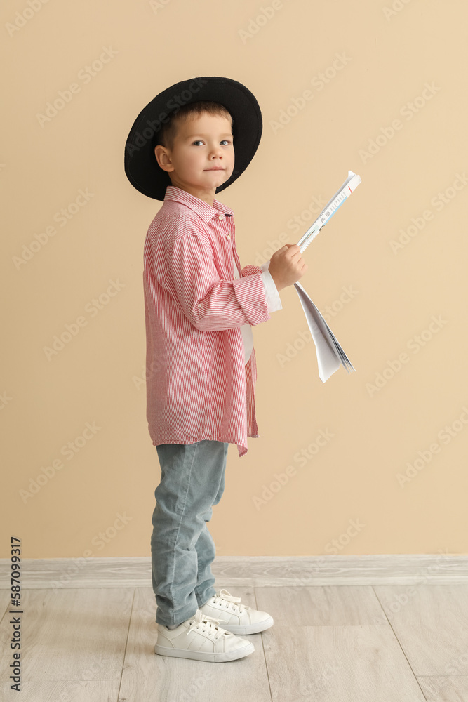 Cute little stylist with newspaper near beige wall
