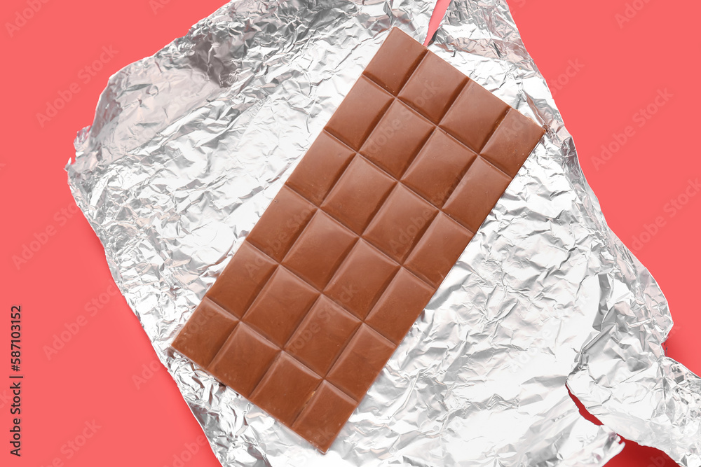 Foil with tasty chocolate bar on red background, closeup
