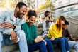 Group of multiracial young people using mobile phone devices sitting outdoors. Millennial happy students addicted to social media app