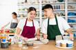© JackF - Smiling young man and woman in aprons making handmade cups of row clay material in pottery workshop