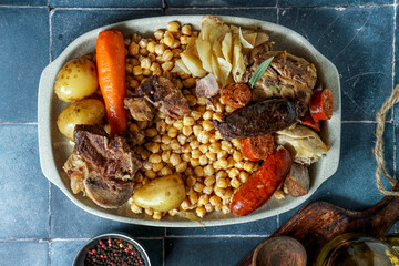 Cocido Madrileño, a traditional Spanish meal, chickpea-based stew from Madrid                          blue ceramic tile background