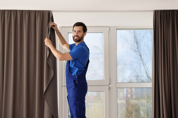 Wall Mural - Worker in uniform hanging window curtain indoors