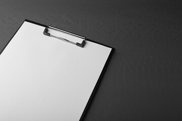Clipboard with sheet of paper on black wooden table. Space for text