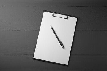 Clipboard with sheet of paper and pen on black wooden table, top view