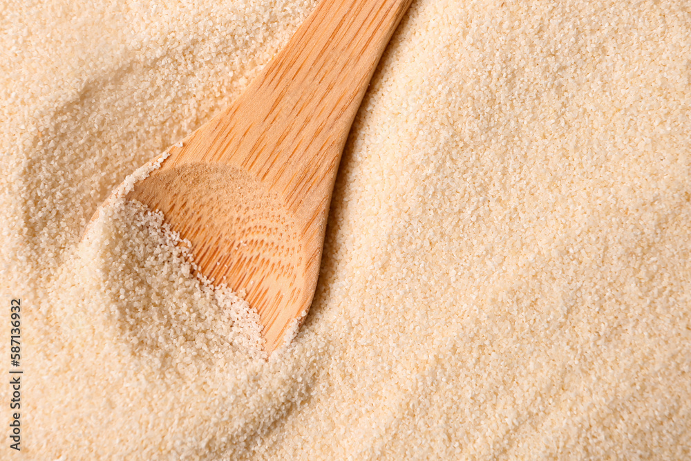 Spoon with raw semolina as background, closeup