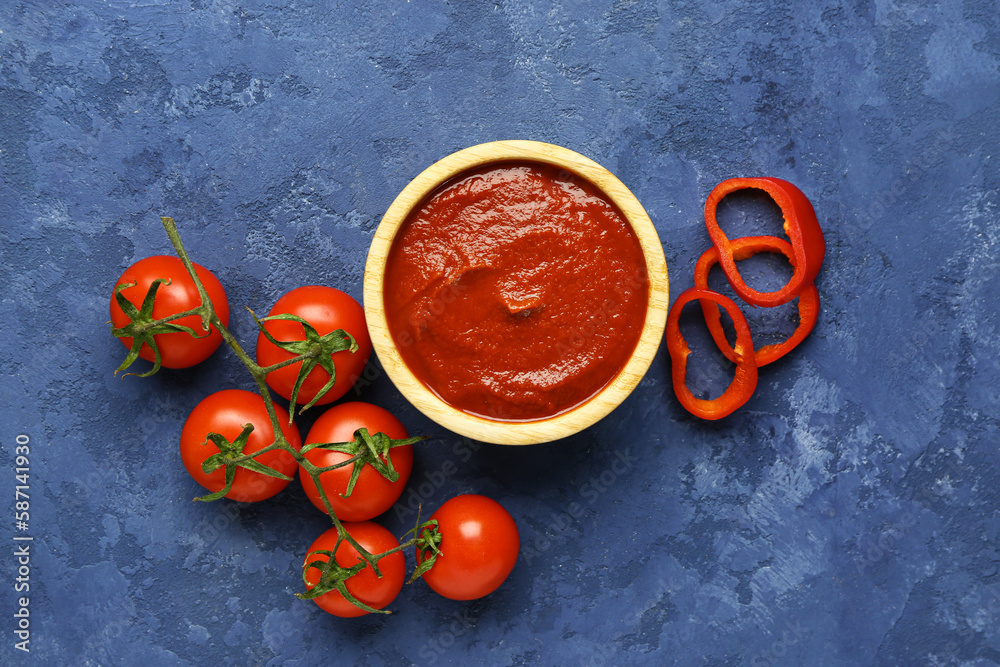 Bowl with tasty tomato paste and fresh vegetables on blue grunge background