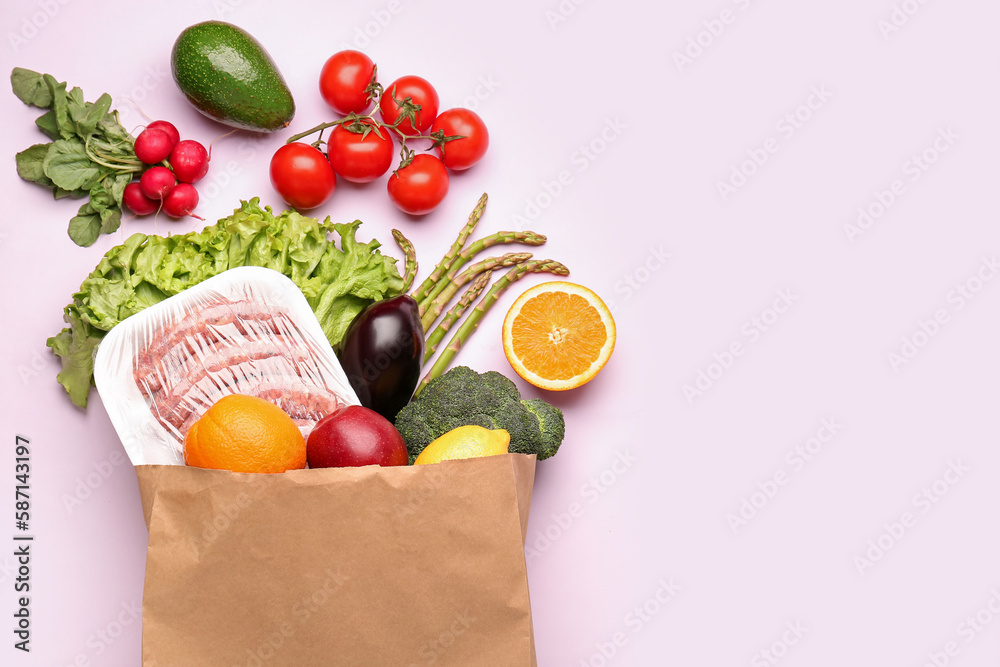 Paper bag with vegetables, fruits and sausages on pink background