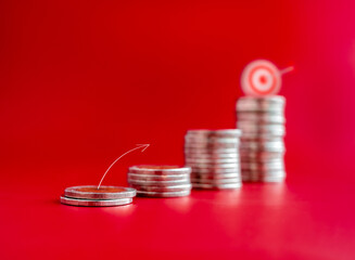 Wall Mural - Close-up arrow line draw jumping to the goal target on the top of coin stacks, graph steps on red background. Investment, saving money, financial income, sales increase, business marketing concepts.