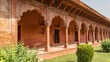 Gallery in the Taj Mahal complex. Terrace, columns, arches made of red sandstone. Wooden doors at the entrance to the premises. Green bushes on the lawn. India. Agra