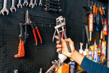 Hands of car mechanic with pliers in garage, tools in the background