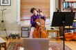 © Cavan Images - A young passionate boy plays cello in front of computer