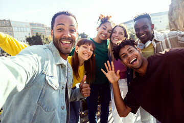 Happy young group of multiracial young friends enjoying time together in city. Diverse student guys and girls having fun taking self portrait during summer vacation