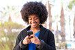 © luismolinero - African American girl at outdoors sending a message or email with the mobile