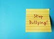 Yellow note stick on blue copy space background with handwritten text STOP BULLYING, stop hurting or frightening others by degrade or demean them in some way just to feel powerful or stronger