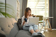 © Prathankarnpap - Happy woman relaxing on couch browsing wireless internet or chatting online on laptop computer