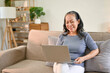 © bongkarn - Cheerful Asian-aged retired woman enjoys watching movie on her laptop in her living room