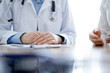 © rogerphoto - Doctor and patient discussing something while sitting near each other at the wooden desk in clinic. Medicine concept