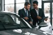 © standret - New plan. Standing near automobile with graphic tablet. Two businessmen are working together in the car showroom