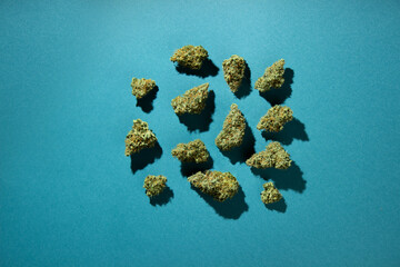 Wall Mural - Dry buds of medical marijuana lie without order on a blue-green background.  Top view, copy space