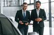 © standret - Near grey colored automobile. Two businessmen are working together in the car showroom