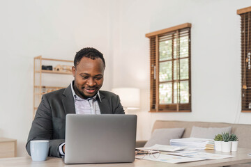 Wall Mural - Focused african american businessman working with laptop documents in office holding papers preparing report analyzing work results, black male analyst doing paperwork at workplace using computer