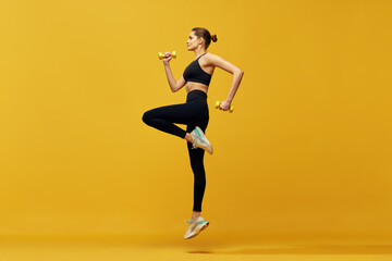 Dynamic image of young beautiful girl in sportswear training, running against yellow studio background. Cardio session. Concept of sport, healthy and active lifestyle, beauty, fitness