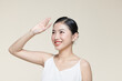 Young asian woman raising hand to covering her face from sunlight against a beige background