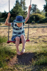 A little boy in a blue hat is having fun on a swing outside