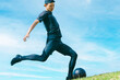 青空の下でサッカーボールを蹴る日本人男性